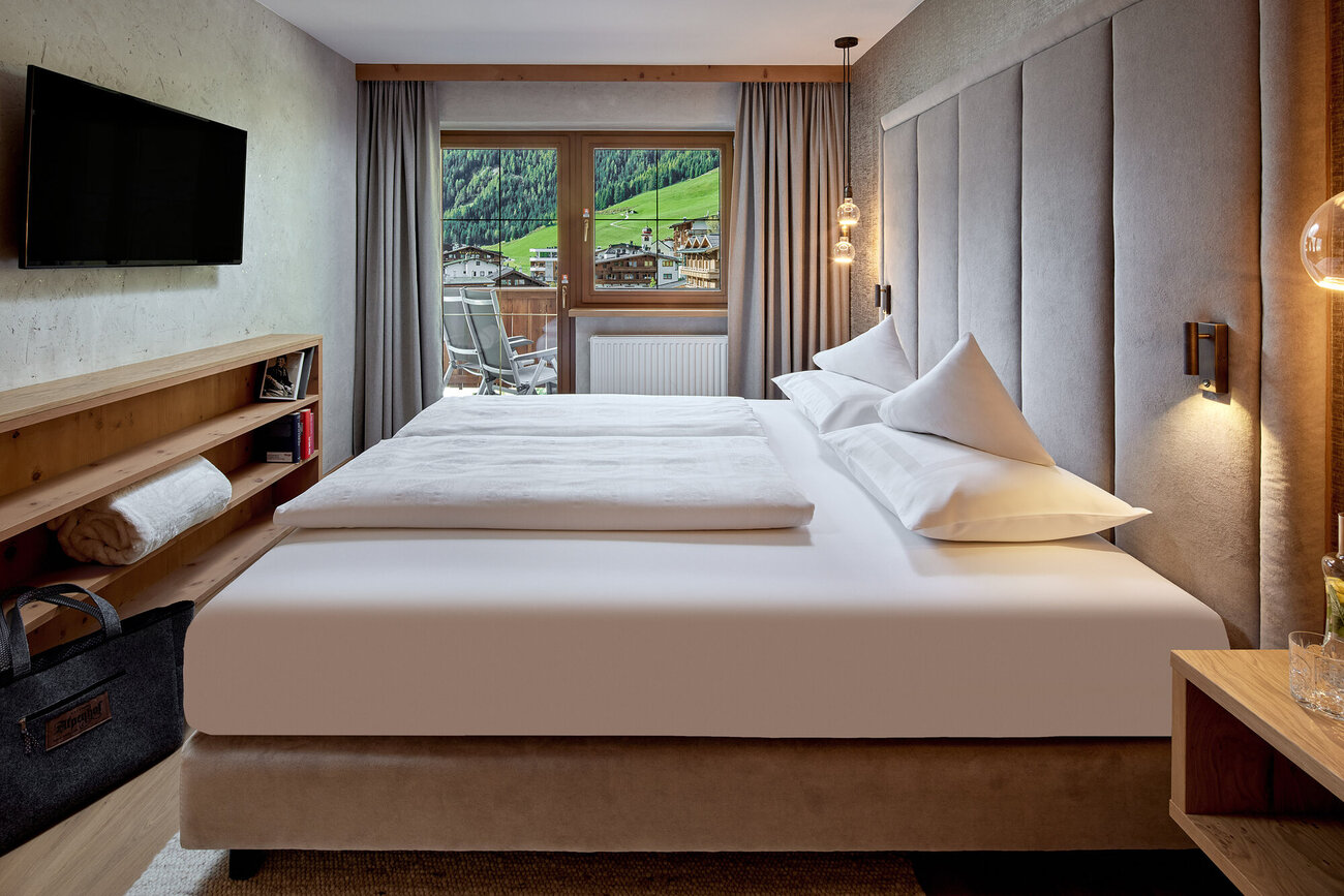 Ein modernes Schlafzimmer mit einem großen Bett, sanften Farben und einem Fenster, das auf eine grüne Berglandschaft blickt.