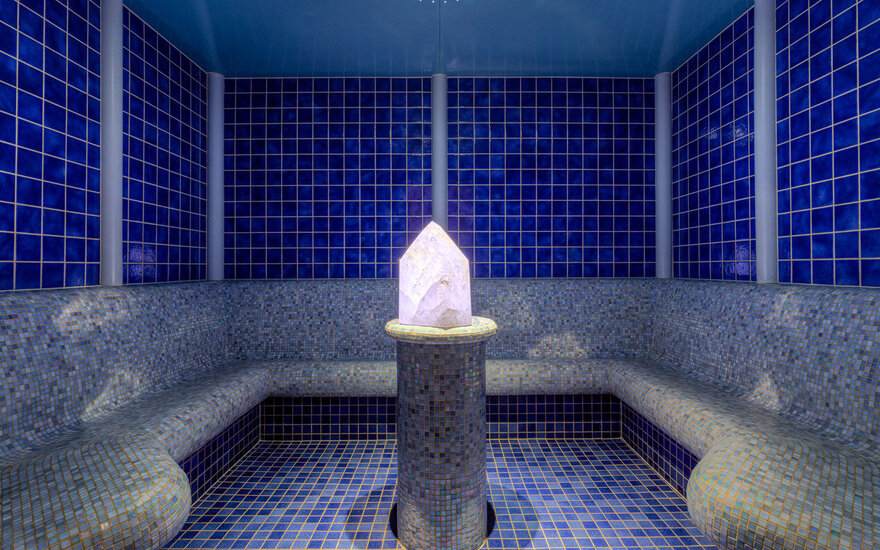 Ein eleganter Dampfbadraum mit blauen Fliesen und einer leuchtenden Kristallskulptur in der Mitte.