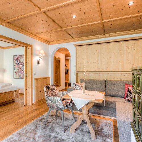 Ein gemütliches Wohnzimmer mit einem Holztisch, einem grauen Sofa und einem dekorativen Ofen in einem modernen alpinen Stil.