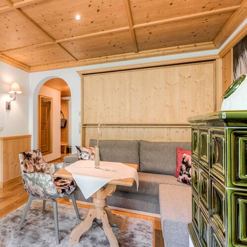 Ein gemütliches Wohnzimmer mit einem Holztisch, einem grauen Sofa und einem dekorativen Ofen in einem modernen alpinen Stil.