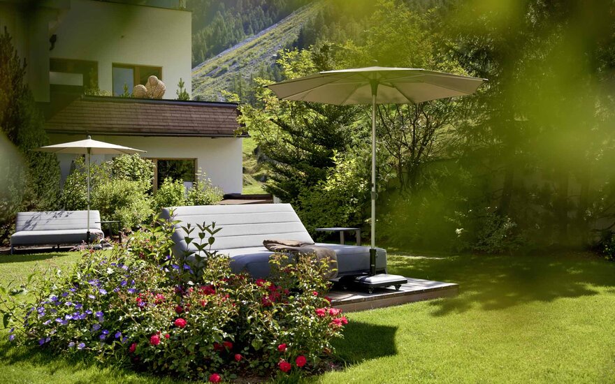 Ein elegantes Liegeplatz im Garten, umgeben von bunten Blumen und einem Sonnenschirm, ideal für Entspannung im Freien.