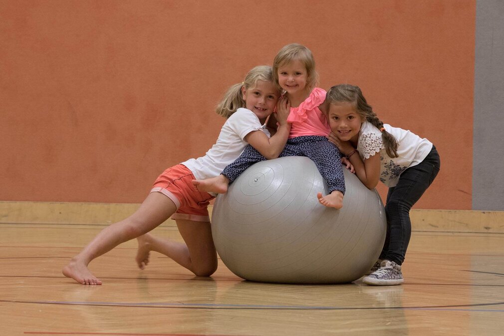 In einer Sporthalle haben drei Mädchen Spaß, während sie auf einem Gymnastikball sitzen und sich gegenseitig umarmen.
