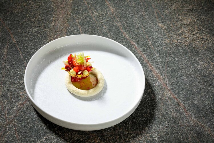 Ein kunstvoll angerichtetes Gericht auf einem weißen Teller, umgeben von einer eleganten, dunklen Steinoberfläche.