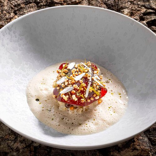 Ein Gourmetgericht präsentiert sich in einer weißen Schüssel, umgeben von einer schaumigen Soße und bunten Toppings.