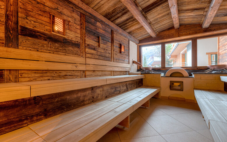 Eine gemütliche Sauna mit Holzverkleidung, großen Fenstern und Blick auf die Berge, die Entspannung und Ruhe ausstrahlt.