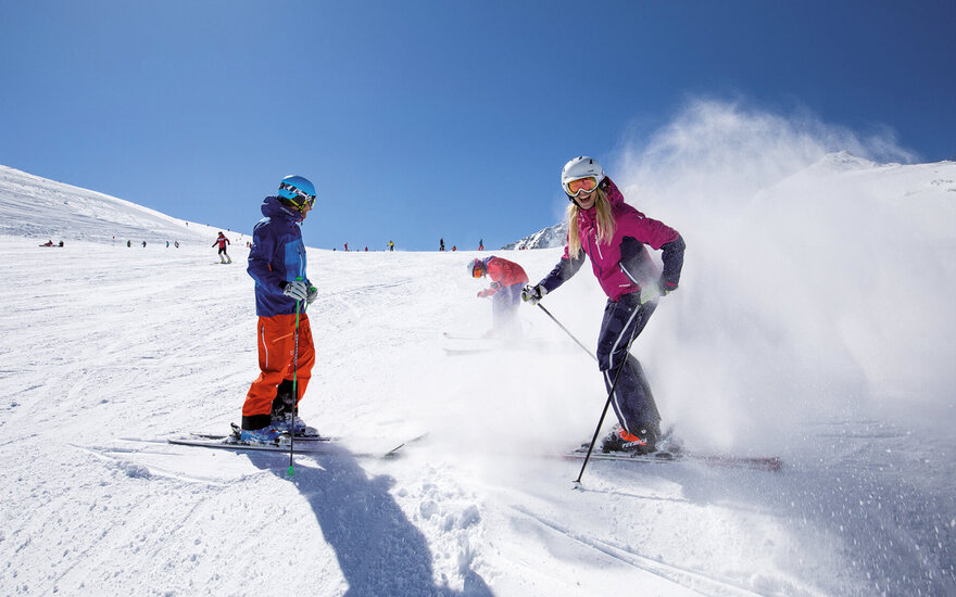Eine fröhliche Skifahrerin in pinker Jacke genießt den Schnee, während sie eine Spur im frischen Pulverschnee hinterlässt.