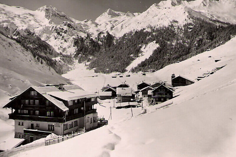 Schneebedeckte Hügel umrahmen ein charmantes Dorf mit Holzhäusern, das in der winterlichen Stille verborgen liegt.