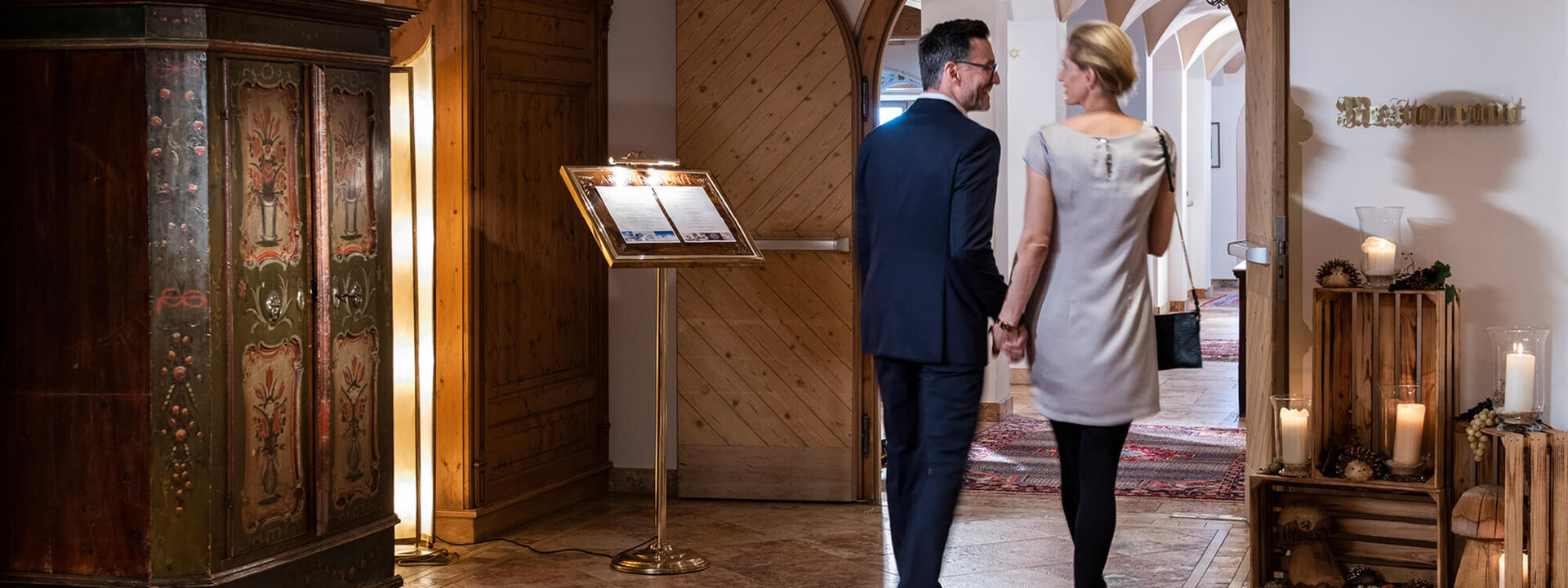Ein Paar hält Händchen und betritt den eleganten Eingangsbereich eines Restaurants mit warmem Licht und stilvollem Dekor.