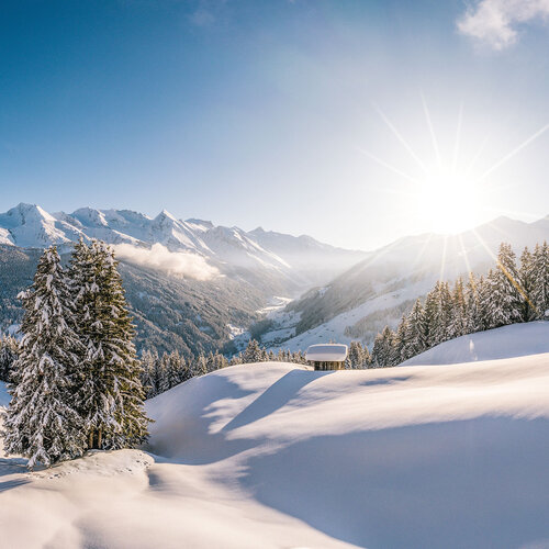 Eine atemberaubende Winterlandschaft mit schneebedeckten Bergen und strahlender Sonne, die über die Hügel scheint.