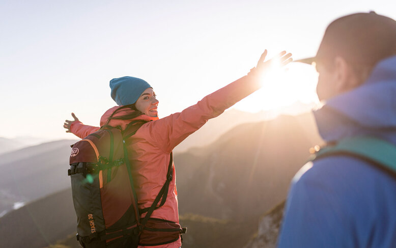Die Wanderin in der pinken Jacke strahlt Freude aus, während sie die Sonne hinter den Bergen begrüßt.