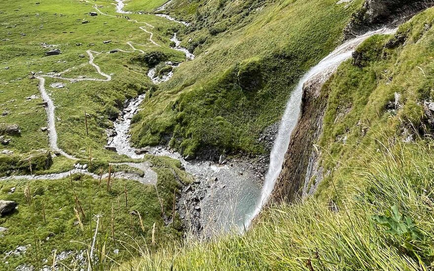 Ein Wasserfall stürzt über eine grüne Klippe, umgeben von saftigem Gras und einem klaren, plätschernden Bach.