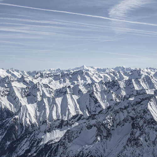 Eine beeindruckende Berglandschaft mit schneebedeckten Gipfeln unter einem klaren blauen Himmel und feinen Wolkenstreifen.