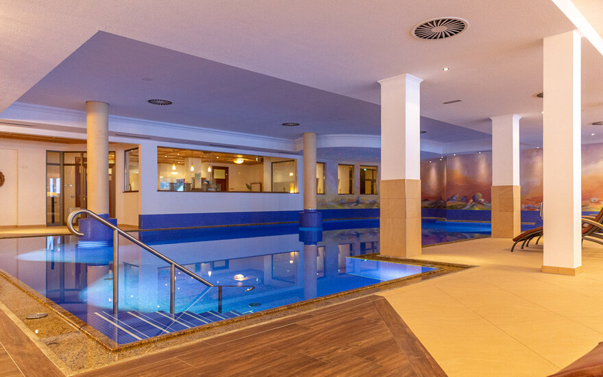 Ein eleganter Innenpool mit blauen Fliesen und einer modernen Treppe, umgeben von stilvollem Ambiente und sanfter Beleuchtung.