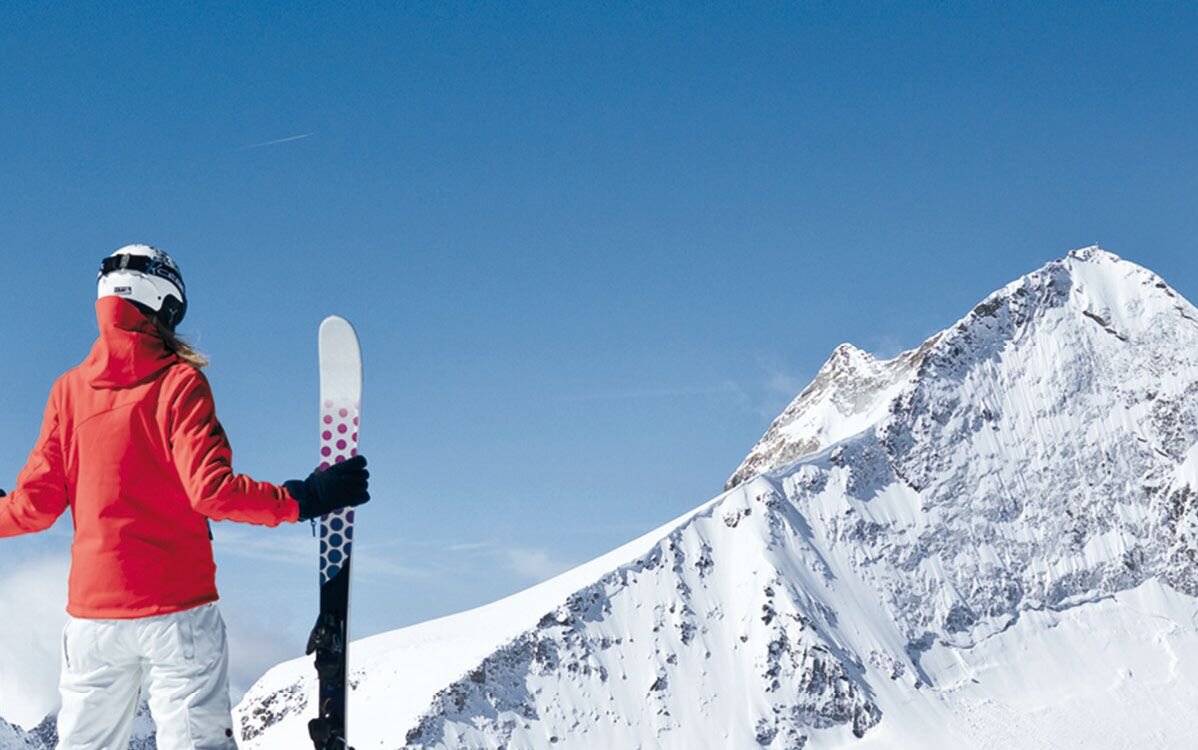 Die Skifahrerin, gekleidet in eine leuchtend rote Jacke, genießt die atemberaubende Aussicht auf die schneebedeckten Berge.