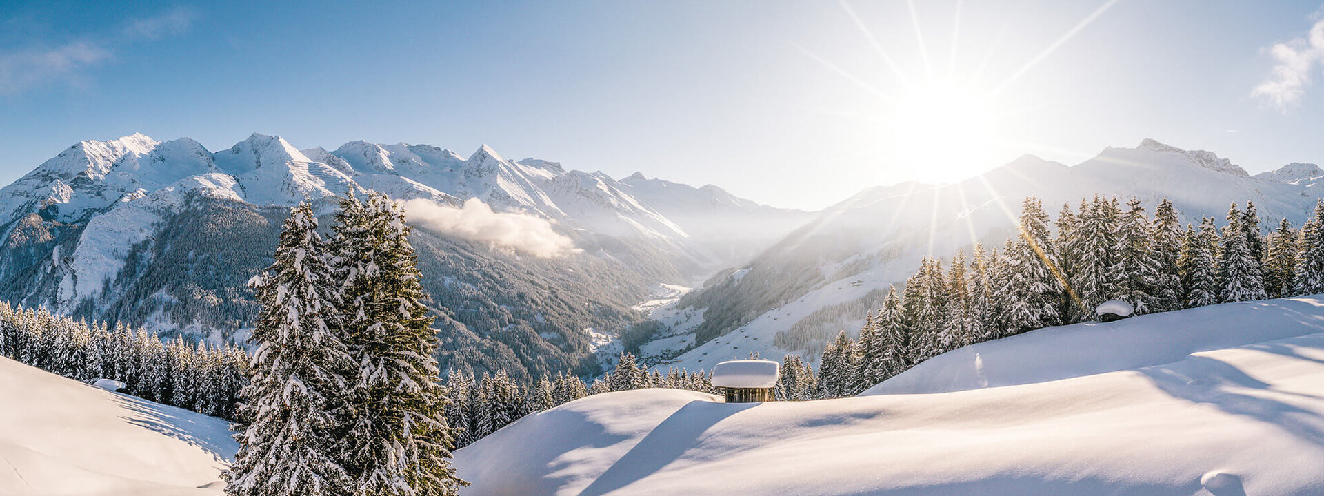 Eine atemberaubende Winterlandschaft mit schneebedeckten Bergen und strahlender Sonne, die über die Hügel scheint.