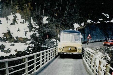 Auf der Brücke fährt ein gelbes Auto, während die schneebedeckte Umgebung und die steilen Felsen eine beeindruckende Kulisse bieten.