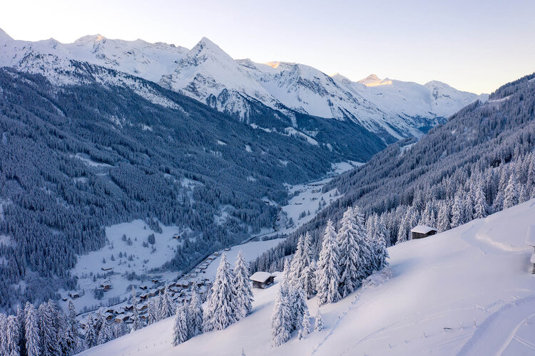 Eine verschneite Berglandschaft mit schneebedeckten Bäumen und einem kleinen Dorf im Tal, umgeben von majestätischen Gipfeln.