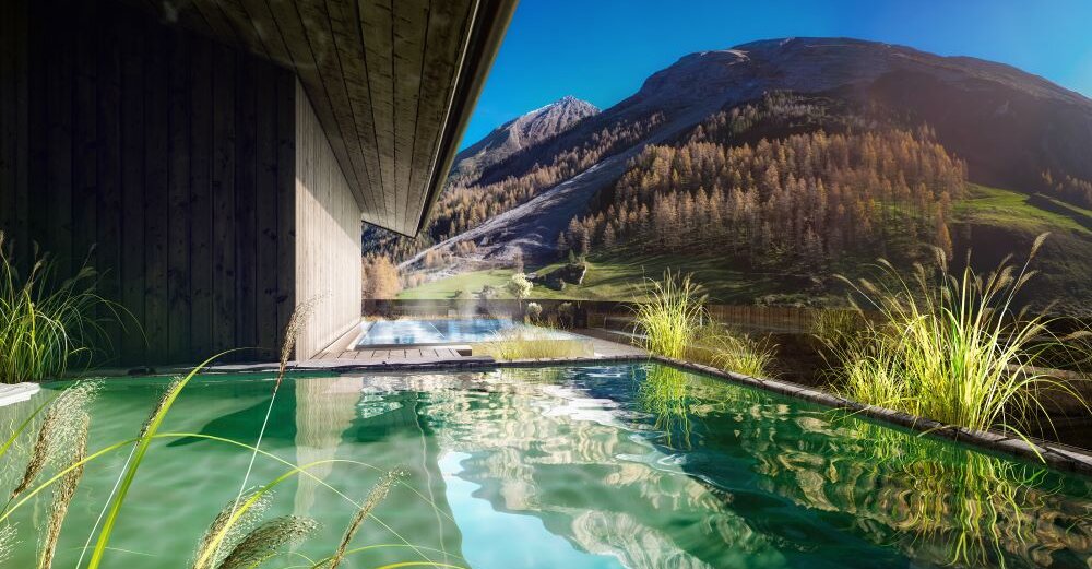 Ein modernes Holzhaus mit einem Pool, umgeben von üppigem Grün und majestätischen Bergen im Hintergrund unter klarem Himmel.