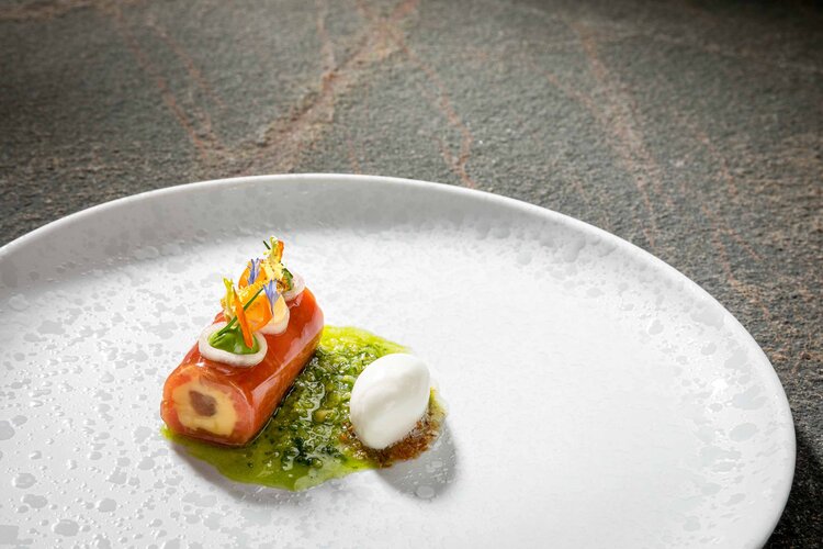 Das Bild zeigt ein kunstvoll angerichtetes Gericht mit einer roten Komponente, frischen Kräutern und einer cremigen Sauce auf einem Teller.