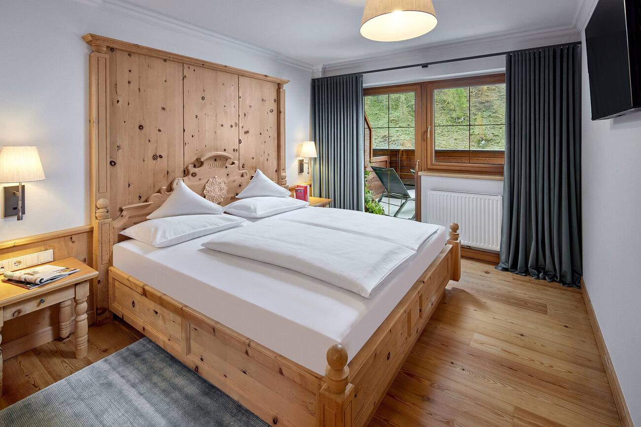 Ein gemütliches Schlafzimmer mit einem großen Holzbett, weißen Kissen und einer warmen Holzverkleidung an der Wand.