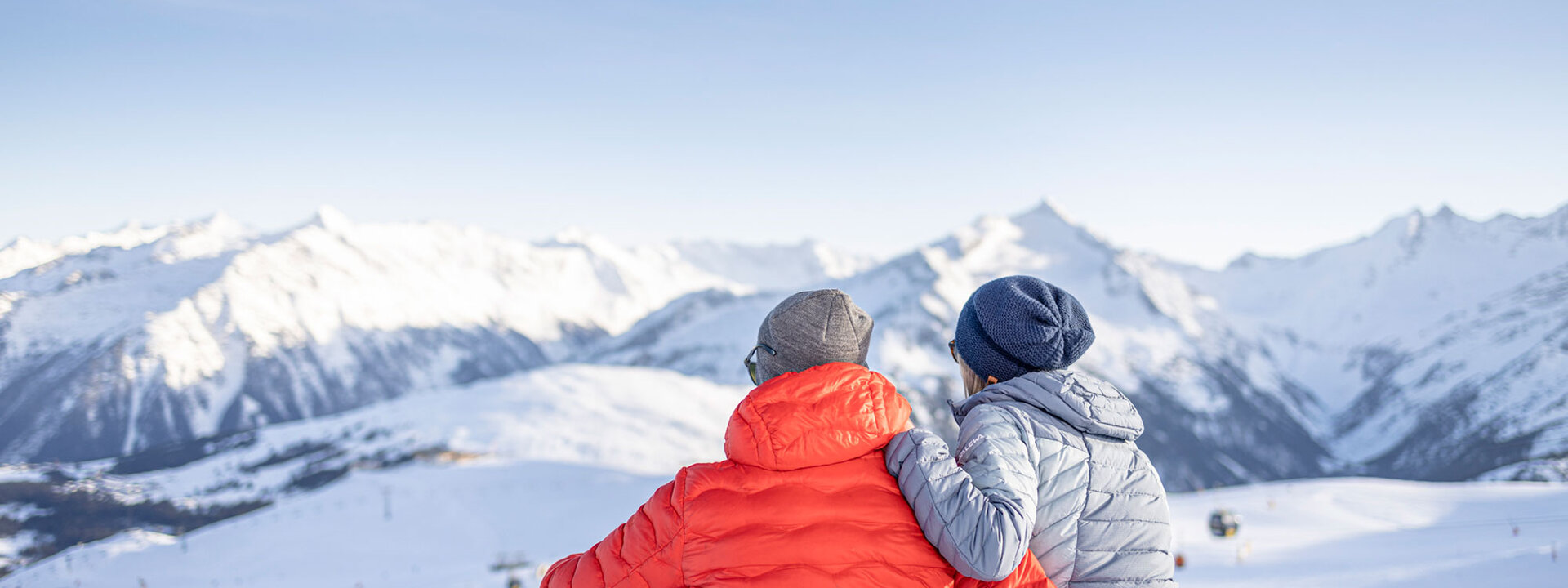 Ein Paar sitzt im Schnee und genießt die atemberaubende Aussicht auf die schneebedeckten Berge im Hintergrund.