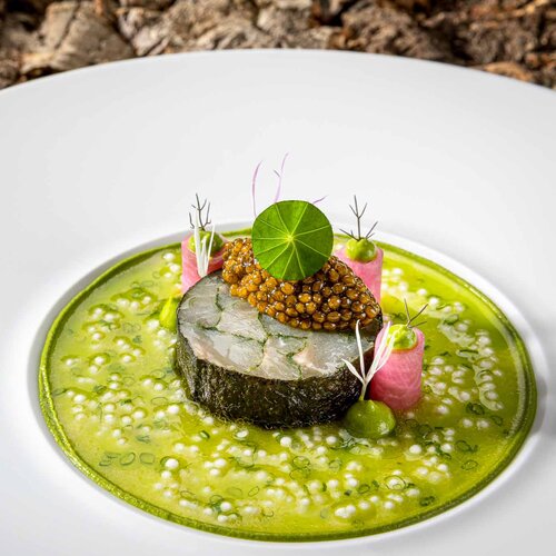 Ein feines Fischgericht, das auf einer grünen Sauce angerichtet ist, ergänzt durch Kaviar und zarte Gemüsestreifen.